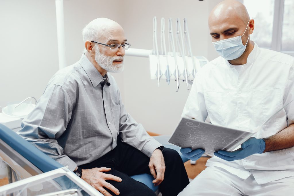 Dentista hablando con un paciente mayor en el consultorio, revisando juntos un documento 