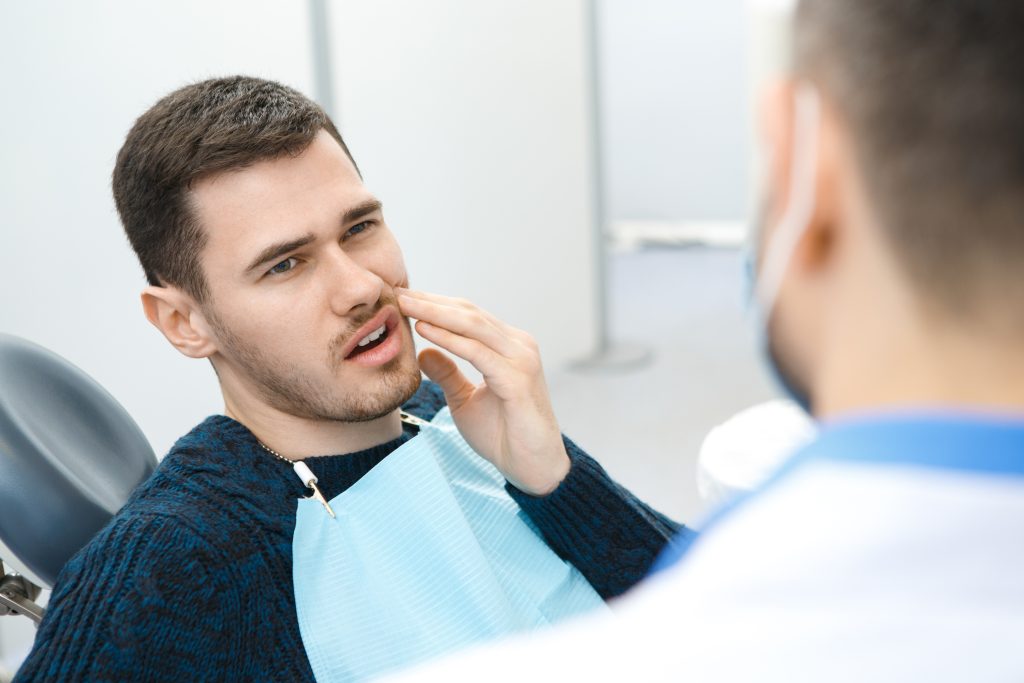 Hombre en el consultorio dental, señalando su mejilla con expresión de dolor