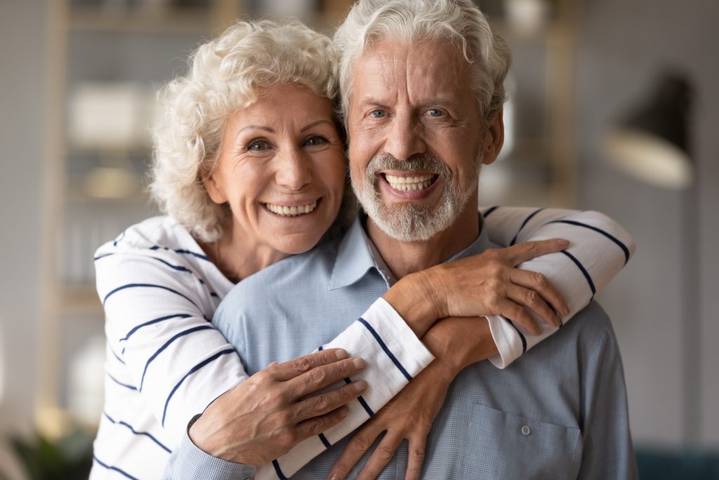 Pareja de adultos mayores sonriendo abrazados.