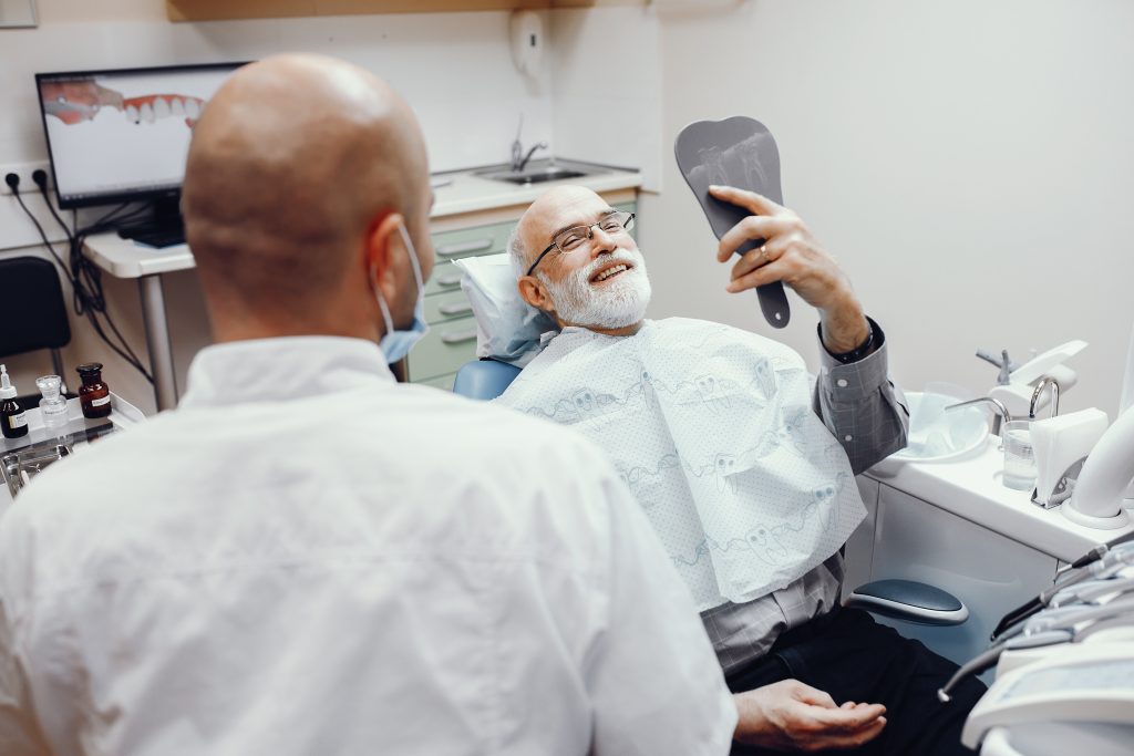 Hombre mayor en el dentista sonriendo mientras se mira en un espejo.